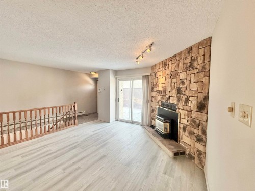 Unfurnished living room with a wood stove, wood finished floors, a textured ceiling, and a baseboard radiator - 2112 104B Street, Edmonton, AB - Indoor With Fireplace