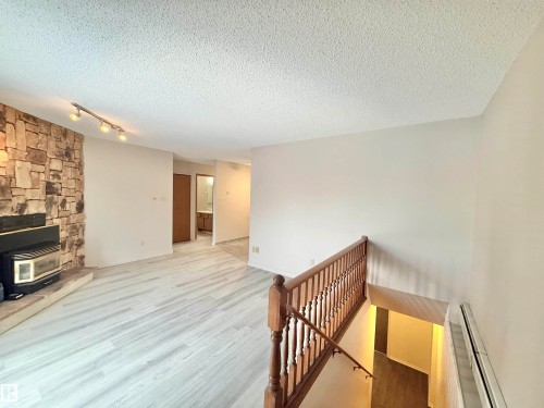 Unfurnished living room with a wood stove, a textured ceiling, a baseboard radiator, and wood finished floors - 2112 104B Street, Edmonton, AB - Indoor Photo Showing Other Room With Fireplace
