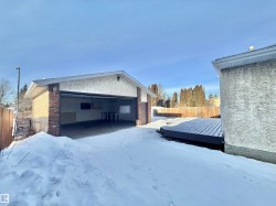 View of snowy exterior featuring stucco siding, a garage, an outbuilding, and a wooden deck - 