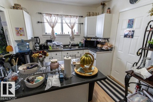 Kitchen with dark countertops, white cabinets, light wood finished floors, and black microwave - 4922 47 Ave, St. Paul Town, AB - Indoor