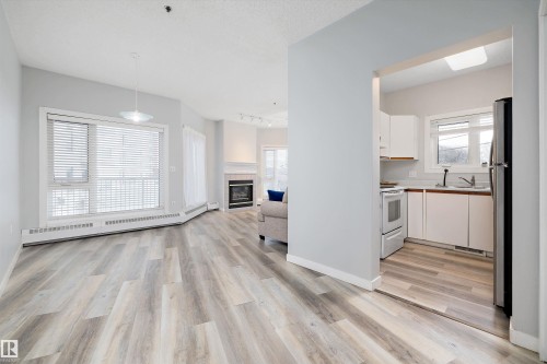 Kitchen featuring white cabinets, light countertops, baseboard heating, open floor plan, and a tiled fireplace - 205 10809 Saskatchewan Drive, Edmonton, AB - Indoor Photo Showing Other Room With Fireplace