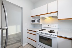 Kitchen with light countertops, white appliances, white cabinets, under cabinet range hood, and brown cabinetry - 