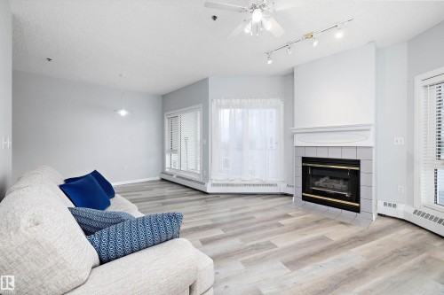 Living area featuring a fireplace, a textured ceiling, light wood finished floors, ceiling fan, and a baseboard radiator - 205 10809 Saskatchewan Drive, Edmonton, AB - Indoor Photo Showing Living Room With Fireplace