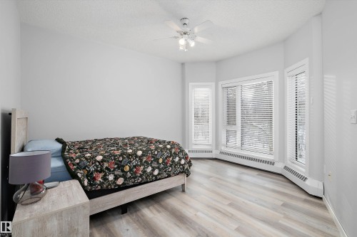 Bedroom featuring a textured ceiling, light wood-style flooring, ceiling fan, and a baseboard heating unit - 205 10809 Saskatchewan Drive, Edmonton, AB - Indoor Photo Showing Bedroom