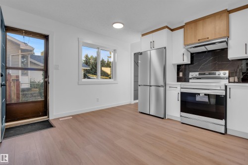 Kitchen featuring white cabinetry, appliances with stainless steel finishes, under cabinet range hood, and backsplash - 1111 49A Street, Edmonton, AB - Indoor Photo Showing Kitchen