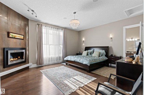 Bedroom featuring dark wood-style flooring, track lighting, a tiled fireplace, and a textured ceiling - 2796 Wheaton Drive, Edmonton, AB - Indoor Photo Showing Bedroom With Fireplace