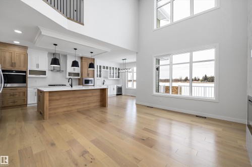 Two tone kitchen featuring two tone cabinetry, pendant lighting, stainless steel appliances, light wood-style flooring, and wine cooler - 230 Edgemont Green Green Nw, Edmonton, AB - Indoor Photo Showing Kitchen