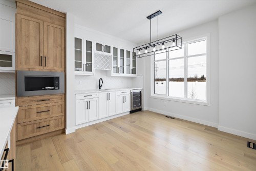 Kitchen with glass fronted cabinets, decorative light fixtures, two tone color scheme, wine cooler, and stainless steel microwave - 230 Edgemont Green Green Nw, Edmonton, AB - Indoor Photo Showing Kitchen
