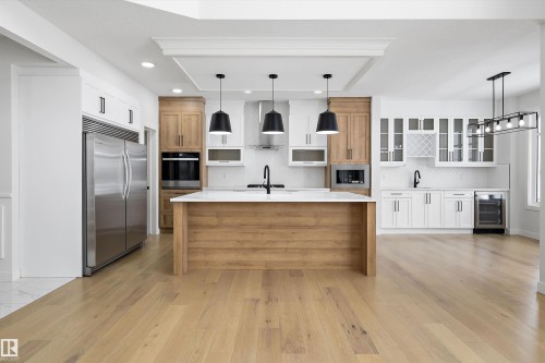 Two tone kitchen featuring two tone cabinetry, built in appliances, pendant lighting, wine cooler, and glass fronted cabinets - 230 Edgemont Green Green Nw, Edmonton, AB - Indoor Photo Showing Kitchen