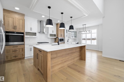 Dual tone kitchen featuring two tone cabinets, glass fronted cabinets, pendant lighting, light stone countertops, and light wood-type flooring - 230 Edgemont Green Green Nw, Edmonton, AB - Indoor Photo Showing Kitchen With Upgraded Kitchen