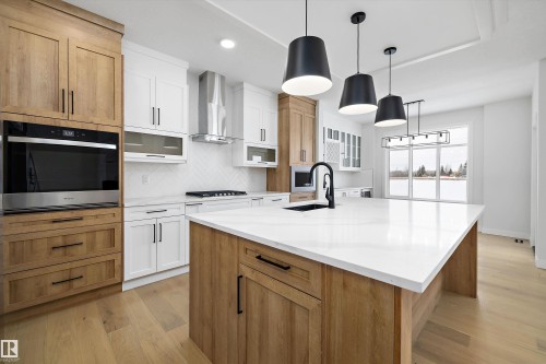 Two tone kitchen featuring two tone cabinetry, light wood-style floors, decorative backsplash, glass fronted cabinets, and stainless steel oven - 230 Edgemont Green Green Nw, Edmonton, AB - Indoor Photo Showing Kitchen With Upgraded Kitchen