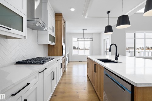 Dual tone kitchen featuring two tone cabinetry, hanging light fixtures, stainless steel appliances, a center island with sink, and light wood-type flooring - 230 Edgemont Green Green Nw, Edmonton, AB - Indoor Photo Showing Kitchen With Upgraded Kitchen