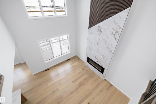 Unfurnished living room featuring healthy amount of natural light, a high ceiling, a premium fireplace, and light wood finished floors - 230 Edgemont Green Green Nw, Edmonton, AB - Indoor Photo Showing Other Room