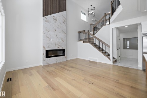 Unfurnished living room with a high end fireplace, a high ceiling, light wood-style floors, and suspended lighting - 230 Edgemont Green Green Nw, Edmonton, AB - Indoor With Fireplace