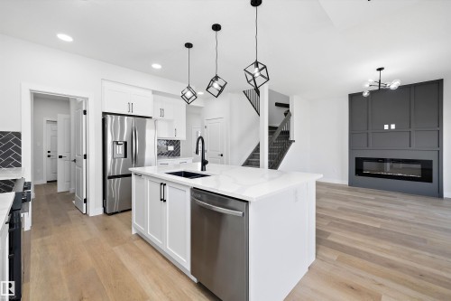 Kitchen featuring stainless steel appliances, a fireplace, light wood-style floors, white cabinetry, and hanging light fixtures - 38 Cannes Cove, St. Albert, AB - Indoor Photo Showing Kitchen With Upgraded Kitchen