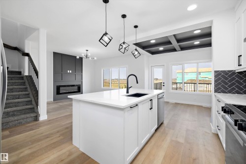 Kitchen featuring coffered ceiling, white cabinetry, light wood-style flooring, open floor plan, and stainless steel appliances - 38 Cannes Cove, St. Albert, AB - Indoor Photo Showing Kitchen With Upgraded Kitchen