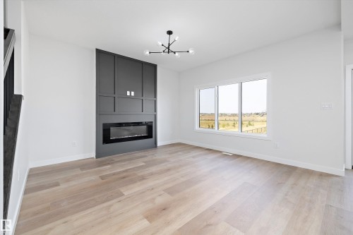 Unfurnished living room with a fireplace, light wood-style floors, and a chandelier - 38 Cannes Cove, St. Albert, AB - Indoor Photo Showing Living Room With Fireplace