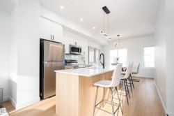 Kitchen featuring appliances with stainless steel finishes, white cabinets, an island with sink, a kitchen bar, and light wood-type flooring - 