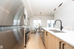 Kitchen with stainless steel appliances, pendant lighting, light wood finished floors, light stone counters, and light brown cabinetry - 