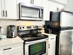 Kitchen featuring appliances with stainless steel finishes, white cabinetry, light stone countertops, and backsplash - 