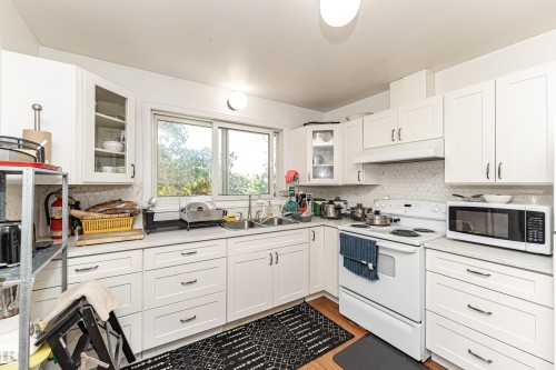 Kitchen with white appliances, white cabinets, glass insert cabinets, and under cabinet range hood - 2349 Millbourne Road W, Edmonton, AB - Indoor Photo Showing Kitchen With Double Sink