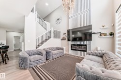 Living area with wood finished floors, a glass covered fireplace, a towering ceiling, stairway, and a chandelier - 