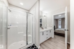 Ensuite bathroom featuring a shower stall, double vanity, light wood finished floors, and recessed lighting - 