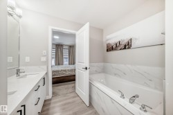 Ensuite bathroom featuring double vanity, a bath, and light wood-style flooring - 