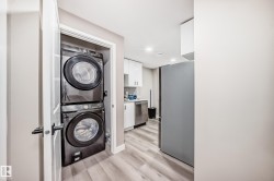 Washroom with stacked washer / drying machine, light wood finished floors, and recessed lighting - 