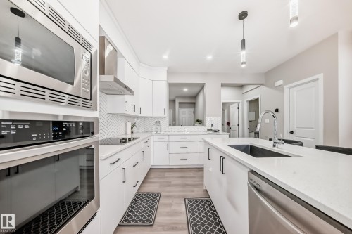 Kitchen featuring hanging light fixtures, appliances with stainless steel finishes, wall chimney range hood, tasteful backsplash, and light wood-style flooring - 4930 Hawthorn Place, Edmonton, AB - Indoor Photo Showing Kitchen With Upgraded Kitchen