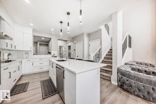 Kitchen featuring light wood finished floors, white cabinetry, backsplash, and hanging light fixtures - 4930 Hawthorn Place, Edmonton, AB - Indoor Photo Showing Kitchen With Upgraded Kitchen