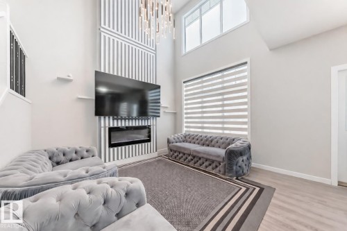 Living room with a glass covered fireplace, a high ceiling, wood finished floors, and a chandelier - 4930 Hawthorn Place, Edmonton, AB - Indoor
