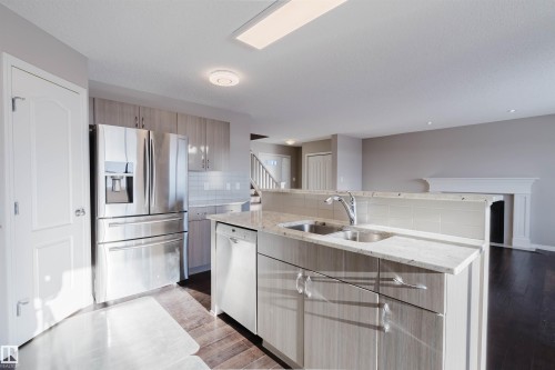 Kitchen with light stone countertops, appliances with stainless steel finishes, decorative backsplash, an island with sink, and light wood finished floors - 16627 18 Avenue, Edmonton, AB - Indoor Photo Showing Kitchen With Double Sink