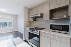 Kitchen with stainless steel appliances, light brown cabinets, under cabinet range hood, light stone countertops, and backsplash - 