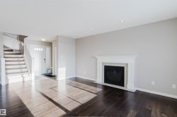 Unfurnished living room featuring dark wood-type flooring, a fireplace with flush hearth, and stairway - 