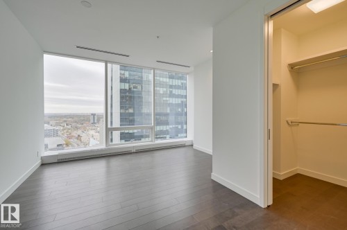 Unfurnished bedroom with a spacious closet, a baseboard radiator, dark wood finished floors, a view of city, and floor to ceiling windows - 2303 10360 102 Street, Edmonton, AB - Indoor Photo Showing Other Room