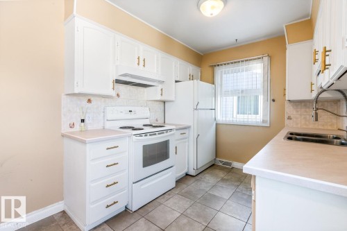 Kitchen featuring white appliances, light countertops, decorative backsplash, white cabinetry, and under cabinet range hood - 7324 77 Street, Edmonton, AB - Indoor Photo Showing Kitchen With Double Sink
