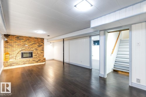 Finished below grade area featuring dark wood-style flooring, stairs, and a brick fireplace - 7324 77 Street, Edmonton, AB - Indoor With Fireplace