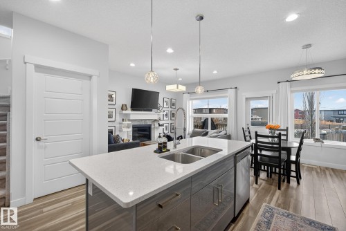 Kitchen featuring open floor plan, a glass covered fireplace, light wood finished floors, light stone counters, and recessed lighting - 17727 13 Avenue, Edmonton, AB - Indoor Photo Showing Kitchen With Fireplace With Double Sink With Upgraded Kitchen