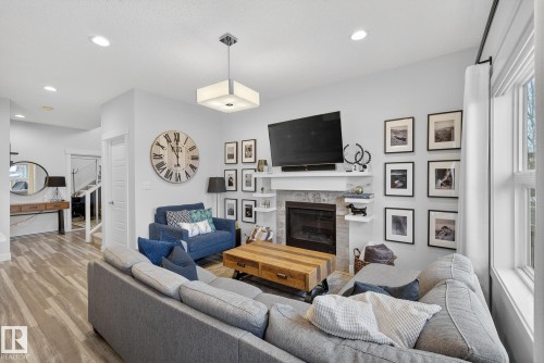Living area featuring recessed lighting, wood finished floors, a glass covered fireplace, and stairs - 17727 13 Avenue, Edmonton, AB - Indoor Photo Showing Living Room With Fireplace