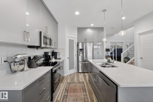 Kitchen featuring gray cabinetry, stainless steel appliances, hanging light fixtures, light wood-style floors, and modern cabinets - 17727 13 Avenue, Edmonton, AB - Indoor Photo Showing Kitchen With Double Sink With Upgraded Kitchen
