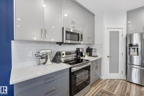 Kitchen with gray cabinetry, stainless steel appliances, backsplash, light wood finished floors, and modern cabinets - 17727 13 Avenue, Edmonton, AB - Indoor Photo Showing Kitchen With Upgraded Kitchen