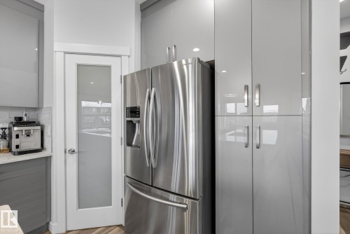 Kitchen featuring gray cabinets, stainless steel fridge, tasteful backsplash, light wood-style floors, and modern cabinets - 17727 13 Avenue, Edmonton, AB - Indoor Photo Showing Kitchen