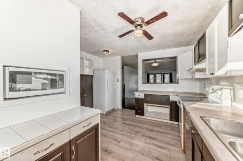 Kitchen with freestanding refrigerator, stainless steel microwave, stove, light wood-type flooring, and a textured ceiling - 131 Saskatchewan Avenue W, Devon, AB - Indoor Photo Showing Kitchen With Double Sink