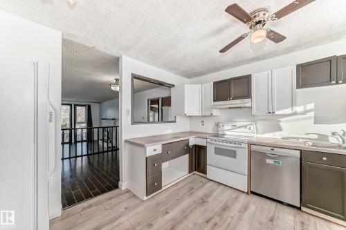 Kitchen featuring white appliances, a textured ceiling, light wood-type flooring, light countertops, and under cabinet range hood - 131 Saskatchewan Avenue W, Devon, AB - Indoor Photo Showing Kitchen With Double Sink