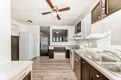 Kitchen with light countertops, white appliances, ceiling fan, a textured ceiling, and dark brown cabinetry - 131 Saskatchewan Avenue W, Devon, AB - Indoor Photo Showing Kitchen With Double Sink