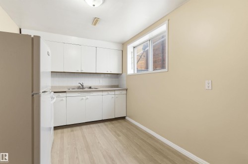 Kitchen with freestanding refrigerator, white cabinetry, light countertops, and light wood-style flooring - 10332 82 Street, Edmonton, AB - Indoor Photo Showing Kitchen With Double Sink