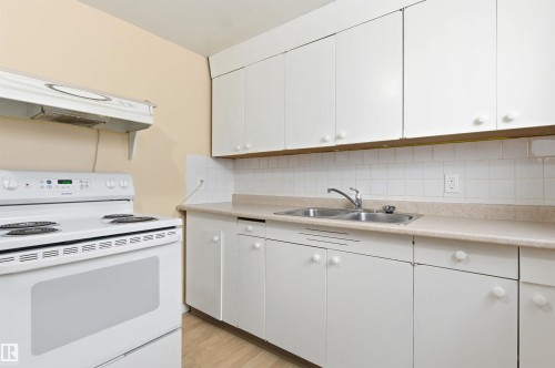 Kitchen featuring white range with electric stovetop, under cabinet range hood, light countertops, and white cabinetry - 10332 82 Street, Edmonton, AB - Indoor Photo Showing Kitchen With Double Sink