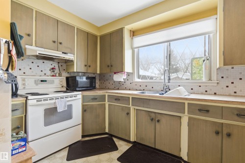 Kitchen featuring white electric range, backsplash, under cabinet range hood, light floors, and light countertops - 10332 82 Street, Edmonton, AB - Indoor Photo Showing Kitchen