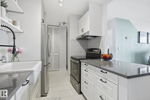 Kitchen with stainless steel appliances, white cabinetry, open shelves, under cabinet range hood, and light tile patterned floors - 1513 13910 Stony Plain Road, Edmonton, AB - Indoor Photo Showing Kitchen